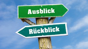 Abbildung eines Wegweisers aus Holz: oben nach rechts weisend ein Schild mit Aufschrift "Rückblick", unten nach links weisend ein Schild mit "Ausblick"