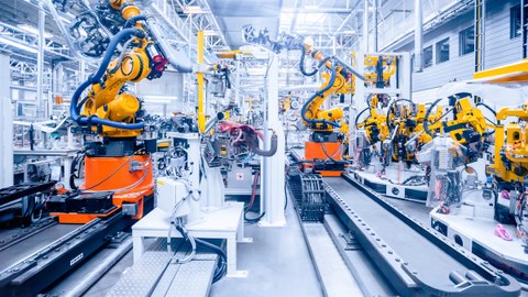 Foto einer großen Halle einer Autofabrik. Auf kurzen Schienen befinden sich große Roboter.