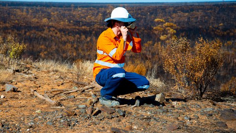 Frau hockt in trockener sonniger Landschaft und untersucht Stein 