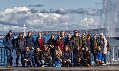 Gruppenfoto der Exkursionsteilnehmer des CERN Ausfluges. Die Studierenden stehen vor einem Geländer. Dahinter befindet sich ein großer See.