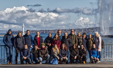 Gruppenfoto der Exkursionsteilnehmer des CERN Ausfluges. Die Studierenden stehen vor einem Geländer. Dahinter befindet sich ein großer See.