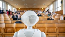 Humanoider Roboter von hinten mit Blick in den Hörsaal.