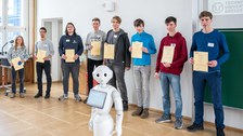 Eine Gruppe zeigt ihre Zertifikate, davor steht ein humanoider Roboter.