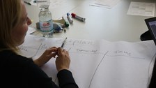 Foto von einer Studentin. Sie sitzt an einem Tisch und schreibt einen Zeitplan auf ein großes Flipchartpapier.