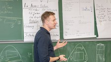 Foto eines Studenten, der vor einer beschrifteten Tafel steht und etwas erklärt.