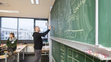 Foto eines Studenten, der vor einer Tafel steht und diese mit Kreide beschriftet.