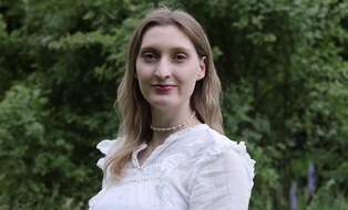 Foto: abgebildet ist ein Porträt von Frau Rowena-Elen Günther, blonde Haare, blau Augen, weiße Bluse
