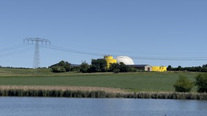 Foto: Biogasanlage  mit Freileitungsmast und Feld sowie See im Vordergrund 