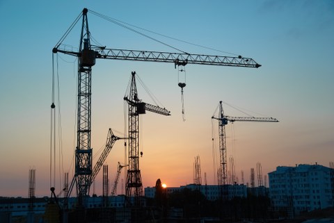 photograph of three tower cranes in the sunset