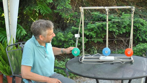 Dr. Michael Kobel setzt ein Pendel, das mit zwei weiteren Pendeln gekoppelt ist, in Schwingung.