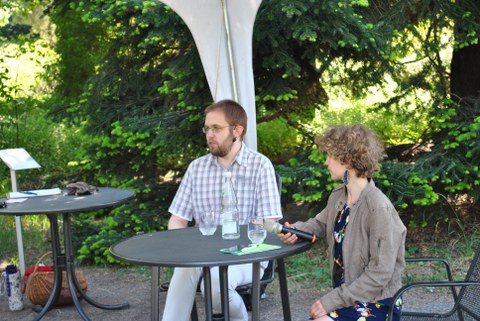 Dr. Malte Schröder und Lilith Diringer sitzen zur Veranstaltung unter einem Partyzelt. Die Bild untermalt die dazugehörige Audio-Aufnahme.