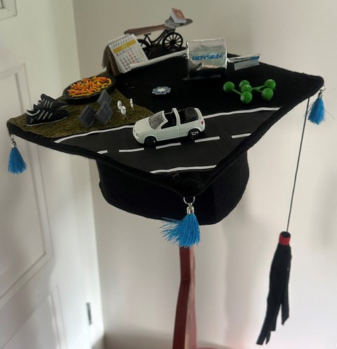 Doktorhut mit diversen kleinen Dekorationen zum Beispiel Solaranlage, Turnschuhe, Kalender und Hanteln