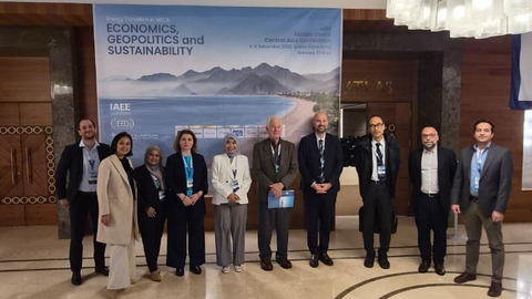 Mehrere Personen stehen in einem weitläufigen Raum. Im Hintergrund ein großes Plakat.