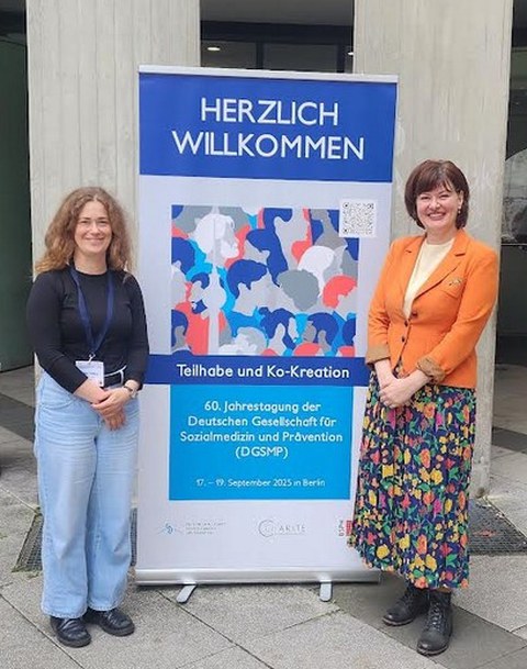 Kollegiatin Linda Ternova und ihre Betreuerin Dr. rer. medic. Alice Freiberg vor einem Aufsteller der Konferenz in Berlin.