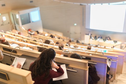 Studierende sitzen in einem Hörsaal und machen Notizen während einer Vorlesung.