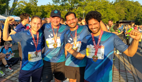 4 Männer blicken lächelnd in die Kamera. Sie tragen alle Medaillen und blaue Laufshirts von der Rewe Team Challenge 2026.