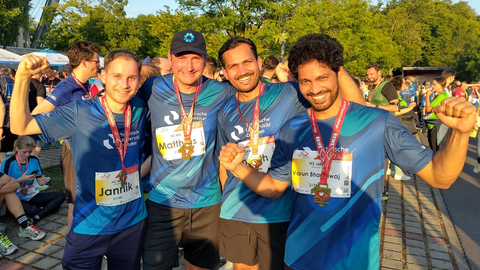 4 Männer blicken lächelnd in die Kamera. Sie tragen alle Medaillen und blaue Laufshirts von der Rewe Team Challenge 2026.