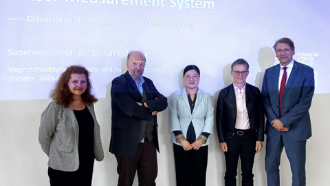 Vier Personen stehen vor einer Wand. Im Hintergrund wird eine Präsentationsfolie auf die Wand projeziert.