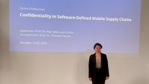 Zarina Chokparova, ehemalige Kollegiatin des 3. Boysen-TUD-GRK, steht vor einer Wand, an der ihre Präsentation gezeigt wird.
