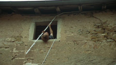 Person misst über Kopf aus einem Fenster heraus eine historische Fassade