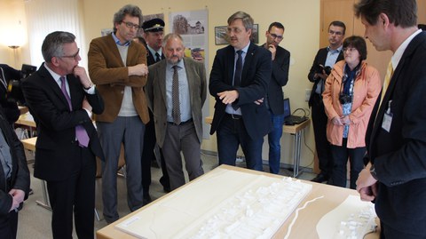 Partner am Forschungsprojekt HUeBro im Gespräch mit Dr. de Maizière vor dem Modell der Dorfanlage