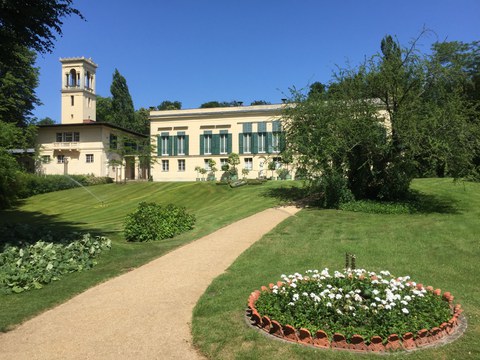 Foto zeigt das kleine Schloss Glienicke auf einer Wiese mit kleinen Gehölzen.