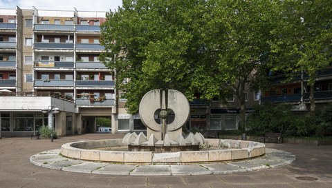 Der Brunnen am Neustädter Markt, im Hintergrund Platanen und Bebauung.