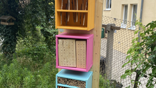 Bild des fertigen Insektenhotels in blau, pink und gelb gestrichen und auf einer Wiese aufgestellt