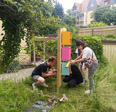 Bild des bunten Insektenhotels und der Studierenden, welche es zur Installation fixieren.