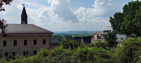 Blick in die Landschaft mit einem Dorf im Vordergrund und Wiesen und WIndrädern im Hintergrund