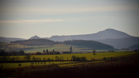 Blick über eine Landschaft mit Kirchturm und Berg im Hintergrund