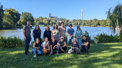 Gruppe von Personen auf einer Wiese vor dem See