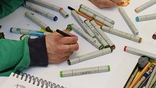 Tisch mit Stiften und Zeichnungen und Studierenden