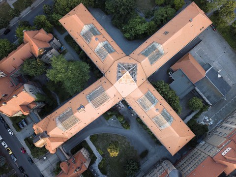 Auf dem Bild ist der Hülße-Bau von oben zu sehen mit siner markanten kreuzförmigen Architektur und rotem Dach.