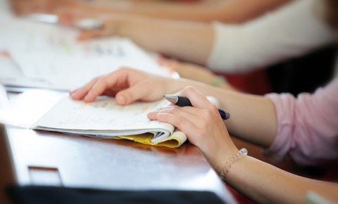 Foto von den Händen einer Studierenden mit einem Notizheft und Stift