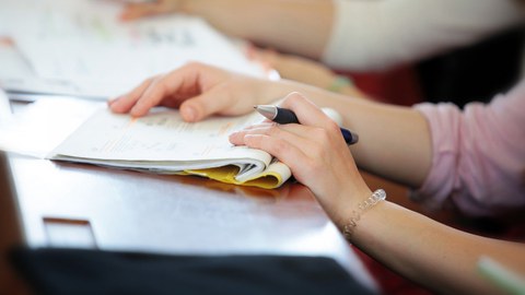 Foto von den Händen einer Studierenden mit einem Notizheft und Stift