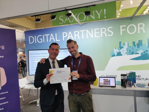 Zwei Männer mit dem Smart-City-Führerschein vor der Standbühne