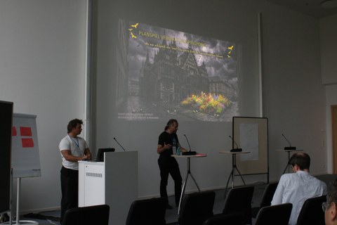 Planspiel auf der Wand im Hintergrund, vorne der Redner
