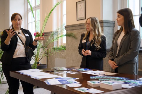 Two women stand at an information stand and give information to a woman