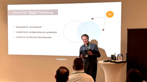 Redner vor Publikum, im Hintergrund Projektion mit Schaubild