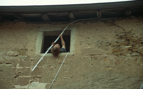 Person misst über Kopf aus einem Fenster heraus eine historische Fassade