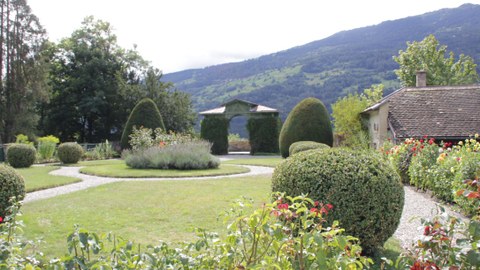 Foto zeigt den Schlosspark Ortenstein in der Schweiz. Das Wegenetz bildet ein Rondell, welches bepflanzt ist. Auf dem Rasen sind geschnittene Buchsbäume angeordnet.