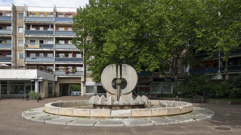 Der Brunnen am Neustädter Markt, im Hintergrund Platanen und Bebauung.