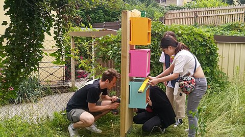 Bild des bunten Insektenhotels und der Studierenden, welche es zur Installation fixieren.