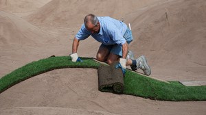 Ein Mann verlegt Rollrasen auf modelliertem Boden.