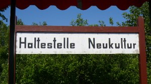 Das Bild zeigt ein Foto einer Bahnhaltestelle mit der Aufschrift "Haltestelle Neukultur".
