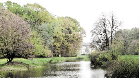 Foto eines Landschaftspark mit Fluss und Herrenhaus dahinter