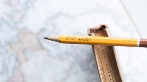 Bild eines auf einem Buch liegenden Bleistiftes, auf dem steht "Study Abroad".