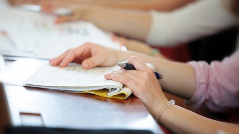 Foto von den Händen einer Studierenden mit einem Notizheft und Stift