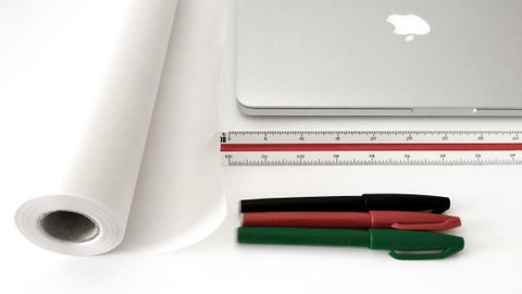 Foto eines Laptops, Lineals, Stiften und einer Pergamentrolle